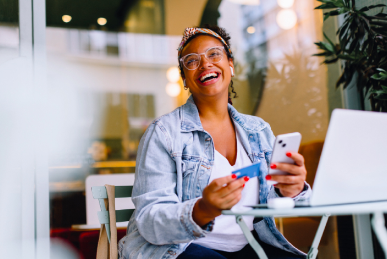 Mulher sorrindo fazendo as contas. Com cartão de banco e smartphone nas mãos.